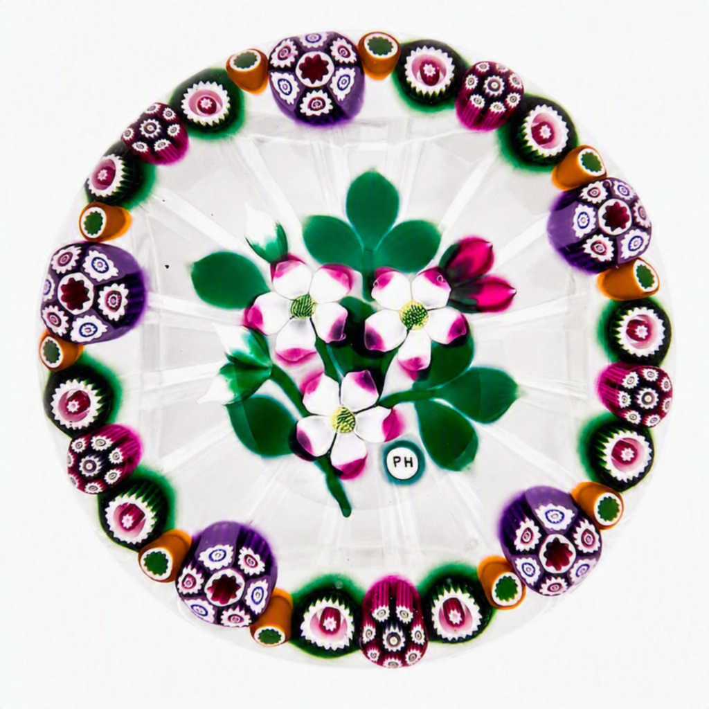 Made in 2025 by Peter Holmes, this Floral Bouquet with Cane Garland is one of my favorites. 3 white and pink flowers with buds, stems and leaves completing a bouquet surrounded by an alternating pattern of 4 distinct designs of complex canes. Clear ground, star cut base, PH signature cane viewed from above. 3.5”