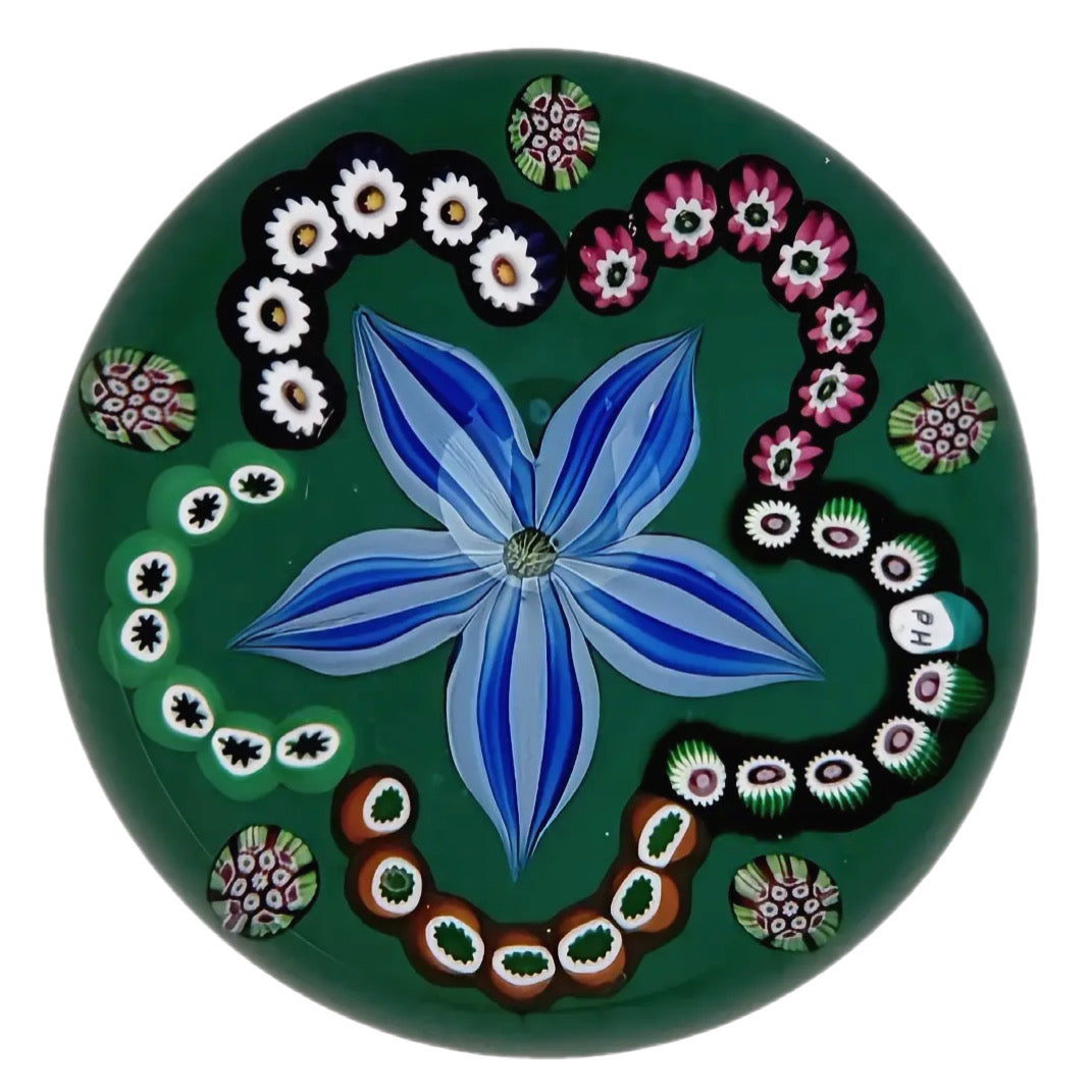 Made by Peter Holmes in 2025 is this handsome, large,&nbsp; a five petaled blue flowerhead surrounded by a millefiori cane garland with 5 identicle complex canes spaced at the garland indentations. scratch signed and dated, PH signature cane. 3 1/8"