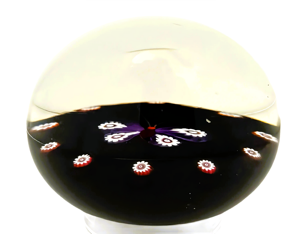 Made by Peter Holmes in 1985 is this purple and white millefiori butterfly atop an&nbsp; opaque black ground. a spaced cane garland with canes identicile to those used for the wings extends around the outer perimeter of the weight.&nbsp; 3" 198/250