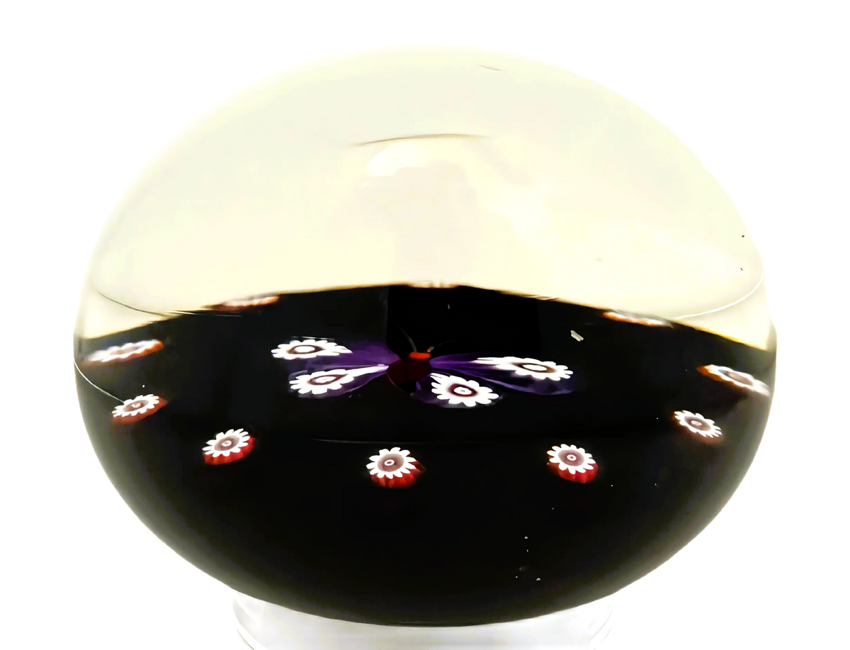 Made by Peter Holmes in 1985 is this purple and white millefiori butterfly atop an&nbsp; opaque black ground. a spaced cane garland with canes identicile to those used for the wings extends around the outer perimeter of the weight.&nbsp; 3" 198/250