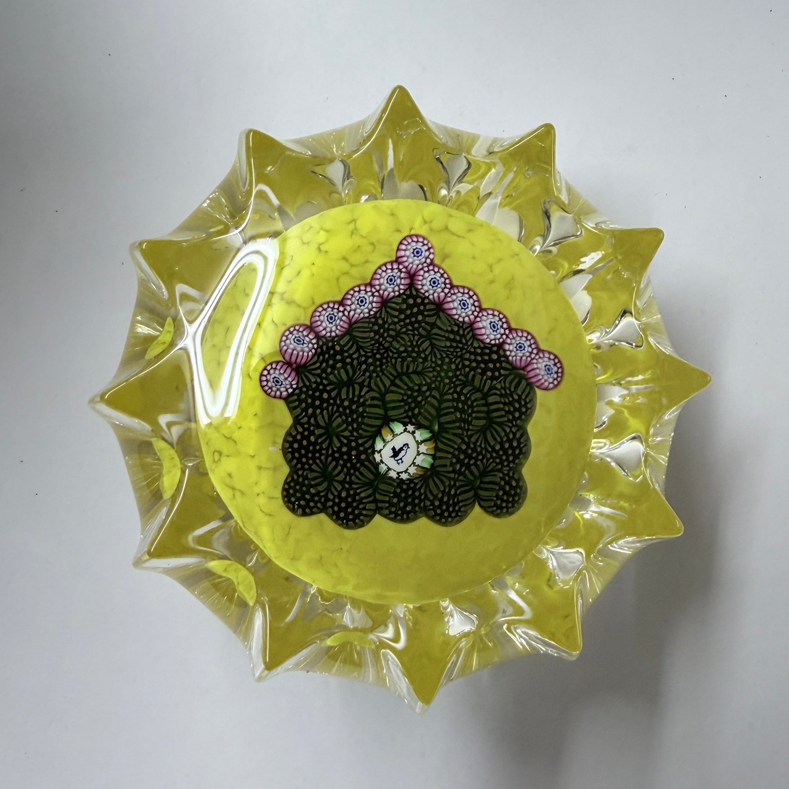 John Deacons Birdhouse 2010 a fun and unusual weight. Different colors of Millefiori arranged in a manner to create a brown birdhouse with pink roof and a bird silhouette atop a fluted yellow ground giving it a sun-like appearance. 2.5"